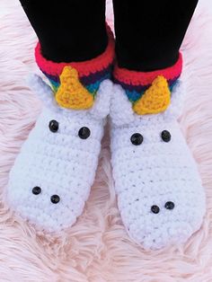 a pair of crocheted slippers with unicorns on them sitting on top of a fluffy pink blanket