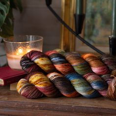 several skeins of yarn sit on a table next to a candle and some books