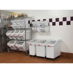 several bins and containers are stacked up in a storage area with tiled walls behind them