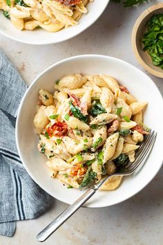 two white bowls filled with pasta and spinach on top of a table next to silverware