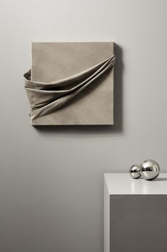 an abstract piece of art hangs on the wall next to a white table with two silver balls