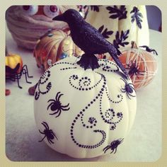 a black bird sitting on top of a white pumpkin decorated with spider webs and beads