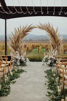 an outdoor ceremony setup with tall grass and flowers on the aisle, surrounded by candles