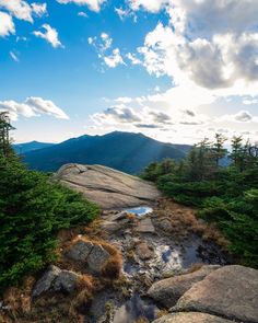 the sun shines on some rocks and trees in the distance, with mountains in the background