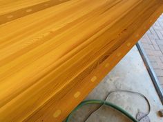 a wooden table sitting on top of a cement floor next to a green hose in front of it