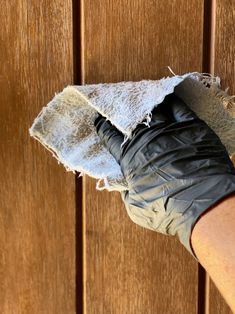 a person's hand wearing black gloves and holding a rag over the top of a wooden door