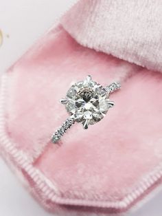 an engagement ring sits on top of a pink velvet case, with the diamond in it's center