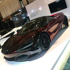 a black and red sports car on display at a showroom with other cars in the background