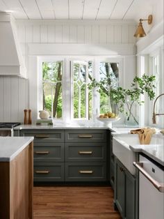 a kitchen with wooden floors and green cabinets, white walls and windows that look out onto the woods