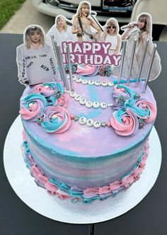 a pink and blue birthday cake with photos on it's top, sitting on a table in front of a car