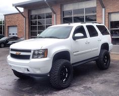 a white truck is parked in front of a brick building with large windows and black rims