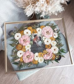 an arrangement of flowers in a glass vase on a table next to a framed photo