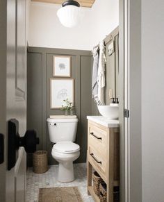 a white toilet sitting inside of a bathroom next to a wooden cabinet and sink under a mirror