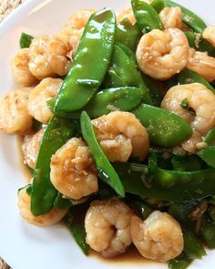 a white plate topped with green beans and shrimp on top of snow snap peas covered in sauce