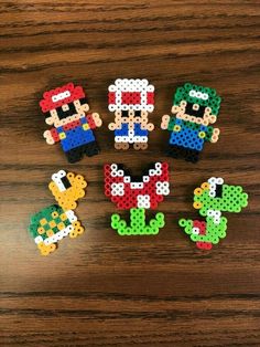 six perler beads are arranged on a wooden surface, including one with an image of mario and luigi