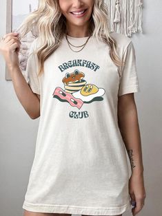 Introducing our Breakfast Club Tee, a must-have addition to your casual wardrobe! Embrace your love for all things breakfast with this charming retro graphic t-shirt. The front design features delightful cartoons of pancakes, eggs, and bacon, creating a nostalgic and whimsical vibe. Crafted with care, this shirt is perfect for brunch enthusiasts, pancake aficionados, and anyone who appreciates a touch of vintage charm. Made from high-quality materials, this Retro Brunch Shirt exudes a hippie-inspired retro aesthetic, blending style and comfort effortlessly. Stand out from the crowd and celebrate the most important meal of the day in true fashion with our Breakfast Shirt - it's a brunch lover's dream come true! Overview -These t-shirts have-ribbed knit collars to bolster shaping. -The shoul Short Sleeve Screen Print Tops For Brunch, Relaxed Fit Cotton Shirt For Brunch, Cotton Shirt With Relaxed Fit For Brunch, Spring Brunch Graphic Print T-shirt, Spring Graphic Print T-shirt For Brunch, Short Sleeve Tops With Funny Print For Brunch, Cotton T-shirt With Letter Print For Brunch, Trendy Cotton Shirt For Brunch, Funny Print Graphic Tee For Brunch