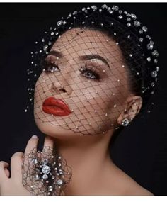 a woman with red lips wearing a veiled headpiece and holding her hand to her face