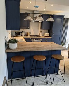 a kitchen with blue cabinets and stools in front of an island countertop that has three hanging lights above it