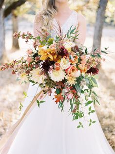 a woman in a wedding dress holding a large bouquet with orange and yellow flowers on it