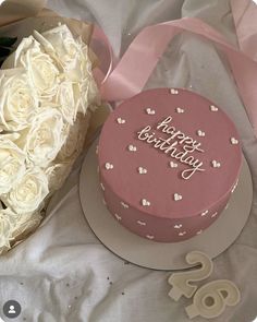 a pink birthday cake and bouquet of white roses