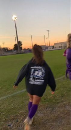 two girls are playing soccer on a field at sunset or dawn, one girl is running with the ball