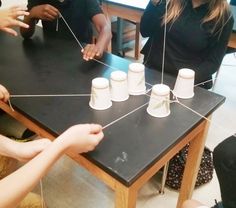 a group of people sitting around a table with cups on top of it and stringing them together