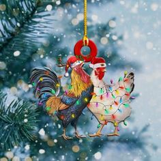 two roosters are hanging from a christmas ornament on a tree in the snow