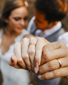 a bride and groom holding hands with gold wedding rings on their fingers in front of each other