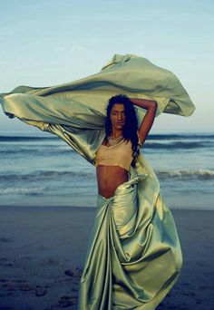 a woman standing on top of a beach next to the ocean wearing a green skirt