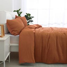 a bed with an orange bedspread and pillows on top of it next to a window