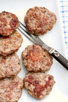 several hamburger patties on a white plate with a knife and fork next to them