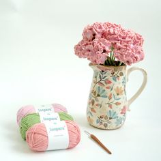 pink carnations in a vase next to a crochet hook and ball of yarn