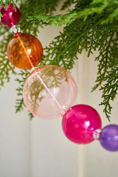 three ornaments hanging from a christmas tree with green leaves and red, pink, purple and orange balls