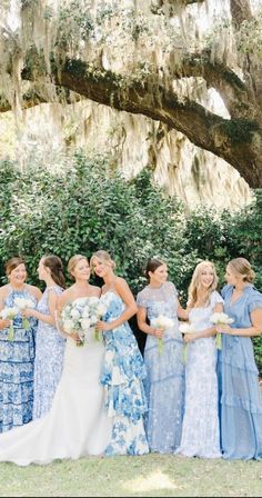 a group of women standing next to each other in front of a lush green tree