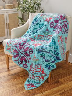 a crocheted blanket sitting on top of a white chair next to a potted plant