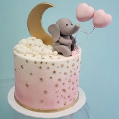 a pink and white cake with an elephant on top holding balloons in the shape of a crescent