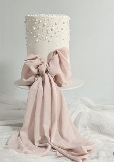 a white and pink wedding cake with pearls on top