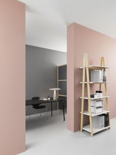 an office with pink walls and white shelving unit in the corner, next to a black desk