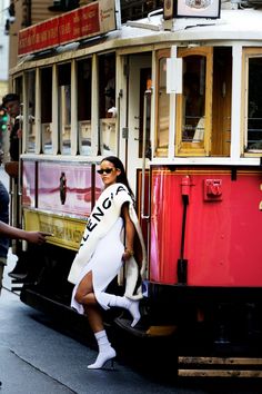 a woman is posing in front of a trolly car on the street while people walk by