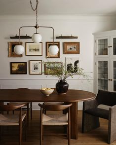 a dining room table with chairs and pictures on the wall above it, along with a vase filled with flowers