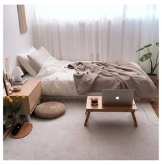 a laptop computer sitting on top of a wooden table next to a bed in a bedroom