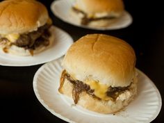 three cheeseburger sandwiches on paper plates sitting on a black table top, ready to be eaten