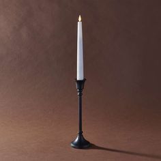 a white candle sitting on top of a black metal stand next to a brown wall