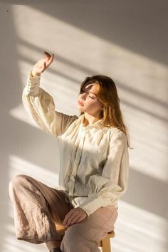 a woman sitting on top of a wooden chair in front of a white wall holding a blue butterfly