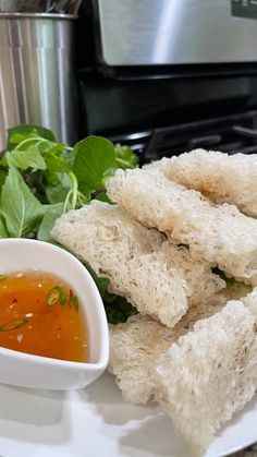 a white plate topped with sandwiches next to a bowl of dipping sauce and green leafy vegetables