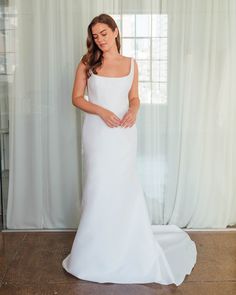 a woman standing in front of a window wearing a white dress and holding her hands on her hip