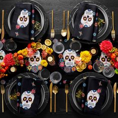 an overhead view of a table set with black plates, silverware and colorful flowers