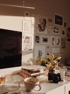 a white desk topped with lots of pictures and a computer monitor next to a plant