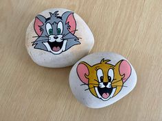 two rocks with cartoon images on them sitting on top of a wooden table next to each other