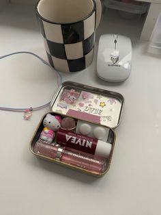 an open tin with various items in it sitting on a table next to a mouse